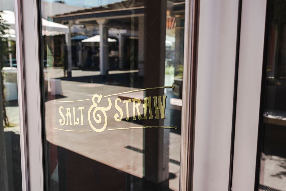 A window decal displays 'Salt & Straw' text with reflections of buildings in the glass storefront.