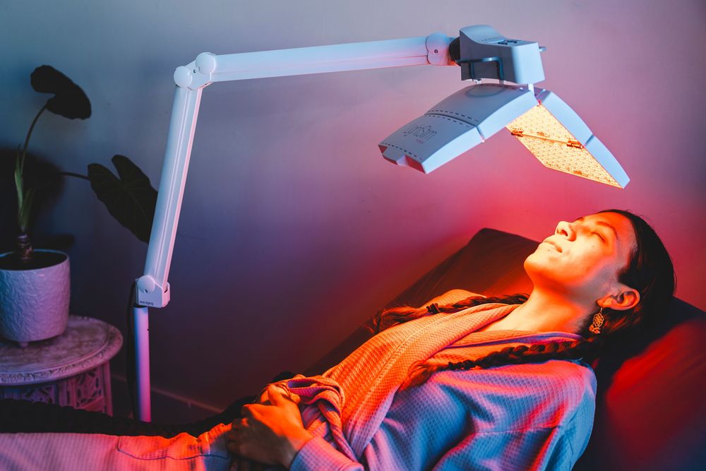 Red and blue LED lights illuminate a medical treatment room during a skincare therapy session.