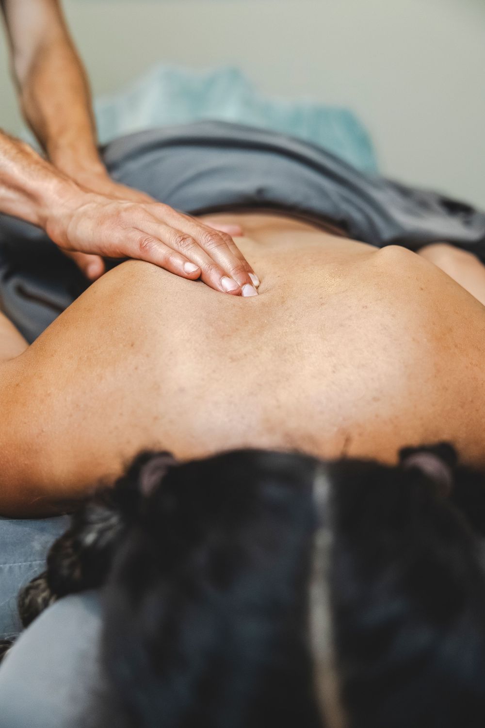 Professional massage therapist performs therapeutic deep tissue back massage on a client lying on massage table.