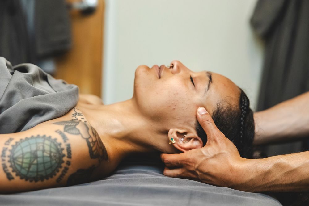 A person lies on a massage table receiving therapeutic treatment with visible tattoos on their arm.