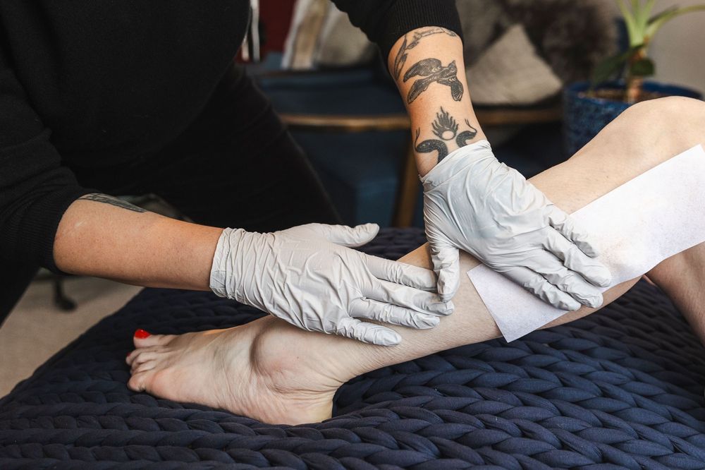 Medical professional in white gloves performs a physical examination of a patient's foot on a dark blue surface.