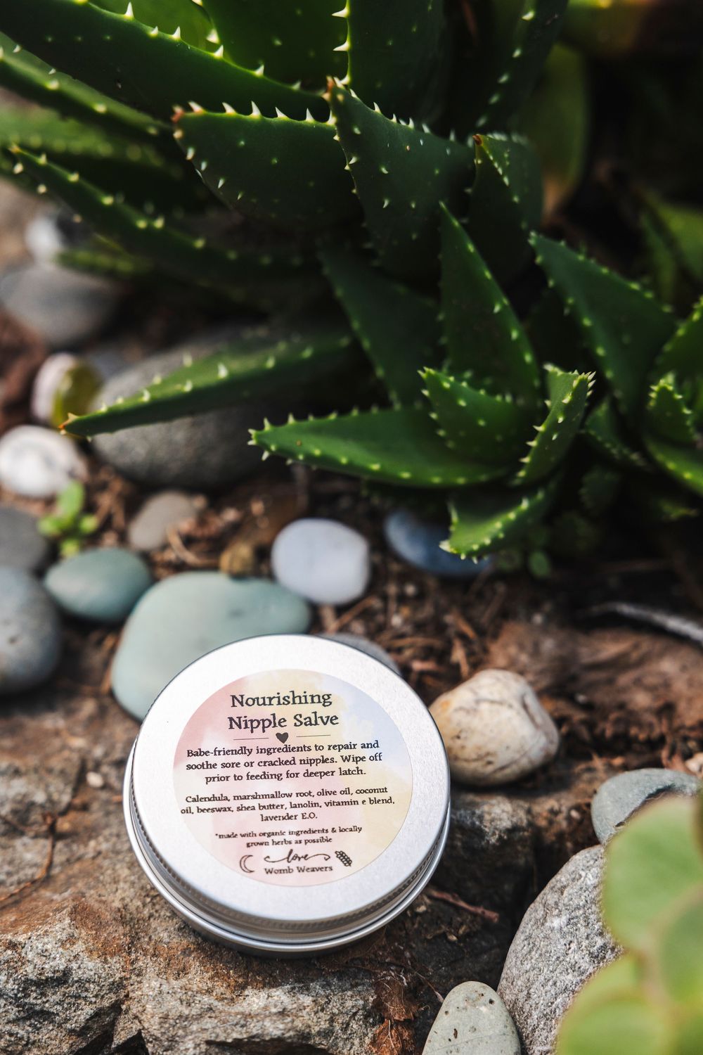 Small metal tins with product labels sit among succulents and decorative stones in a garden setting.