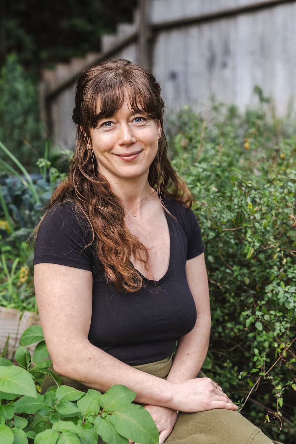 A person in a black shirt sits outdoors near green foliage in a garden setting.