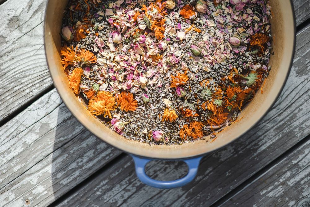 Colorful birdseed mixture with dried flowers and grains displayed in a round ceramic bowl on wooden deck planks.