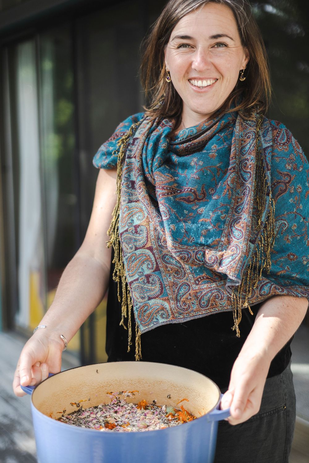 A person wearing a blue patterned scarf stirs a large pot of food while cooking in a kitchen setting.