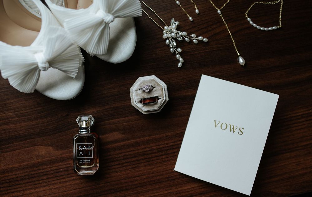 Wedding rings and vows book arranged on dark wooden surface with white bow details.