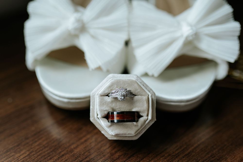 Close-up of elegant wedding rings displayed with white ribbon on dark wood surface.