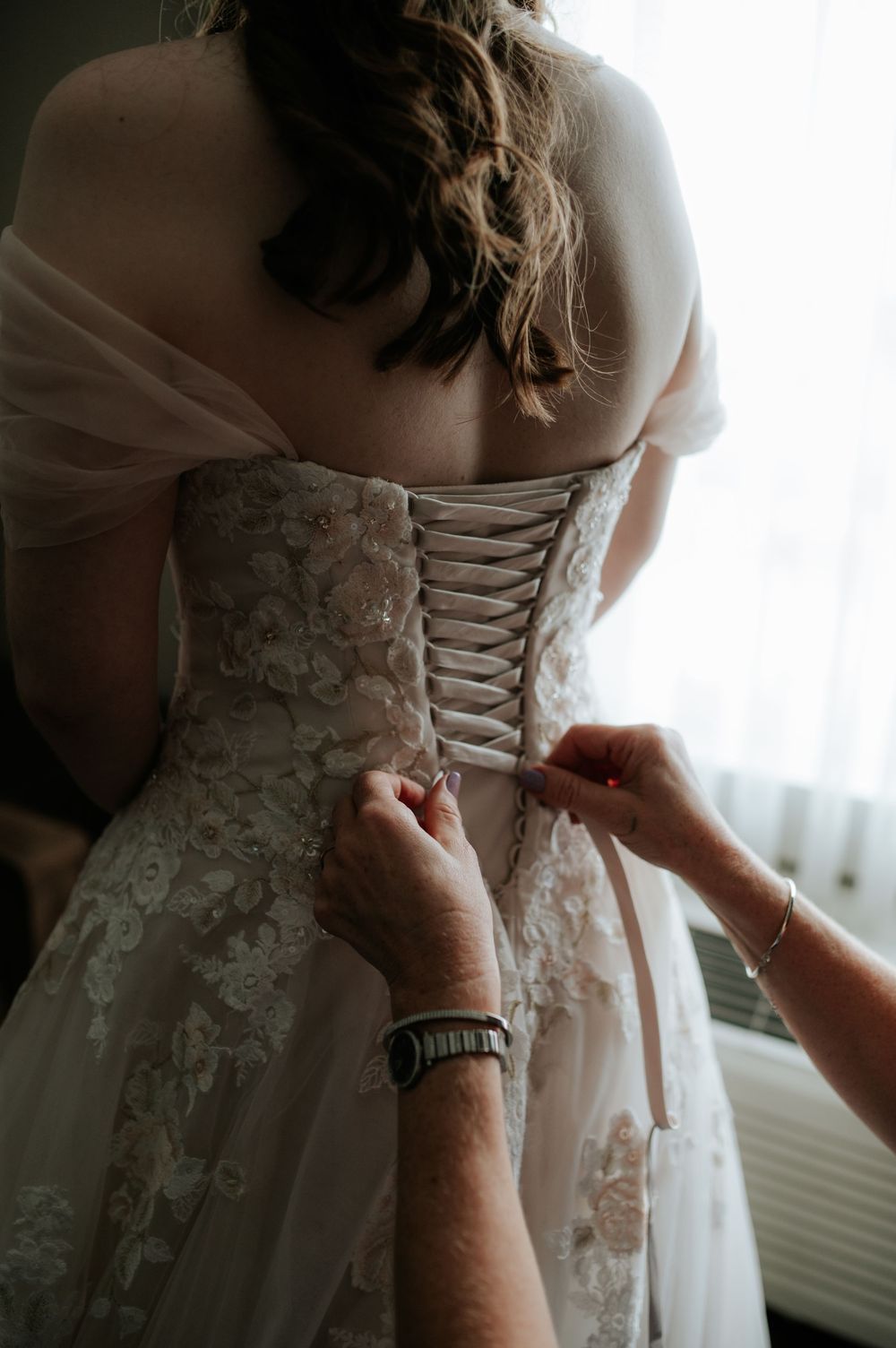 Detail shot of intricate lace wedding dress being laced up in corset style.