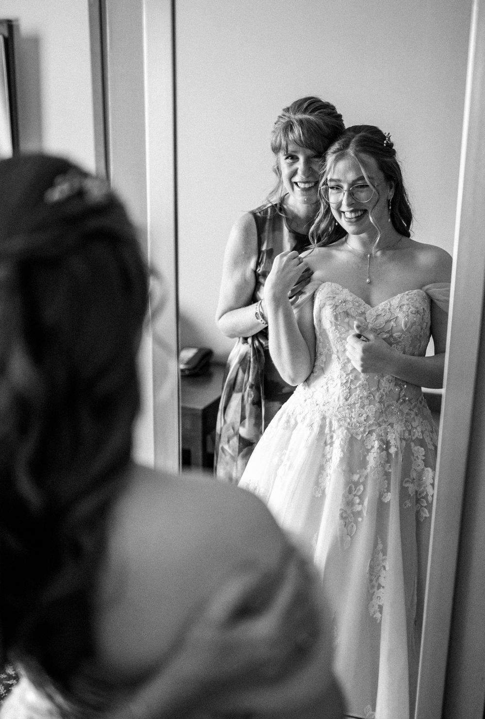 A black and white photo of final wedding dress preparations in front of a mirror.