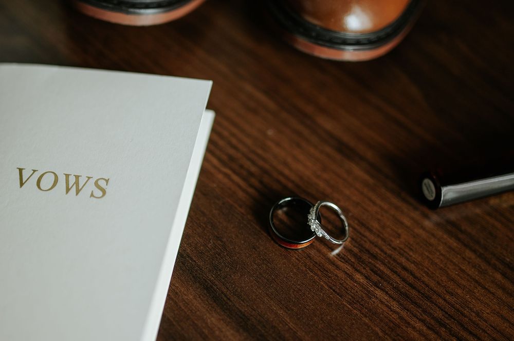 Wedding vows book and gold rings displayed on dark wooden surface with soft lighting.