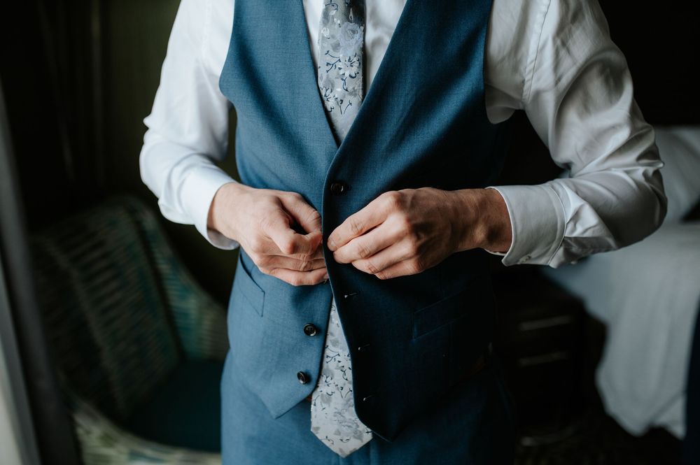 Close-up details of formal blue suit and tie adjustments during wedding preparations.