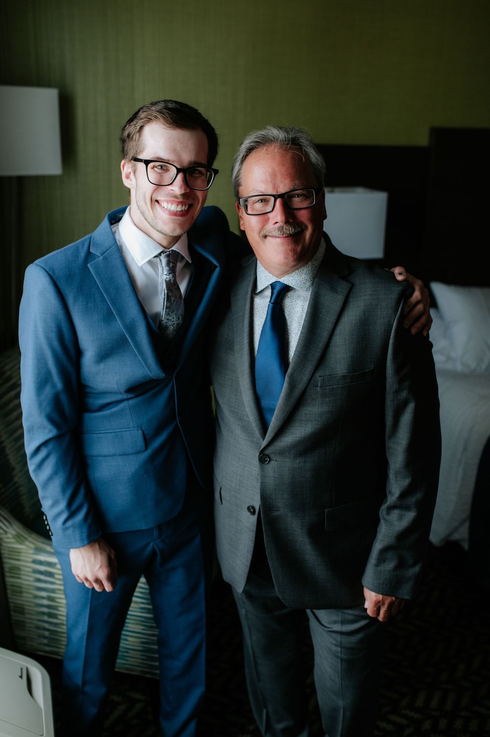 Two people in formal attire, one in blue suit and one in grey suit, posing together.