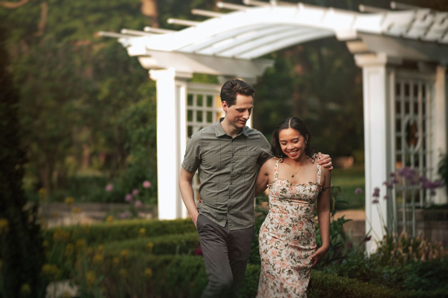 A couple walking a garden photoshoot with a white gazebo in the background.