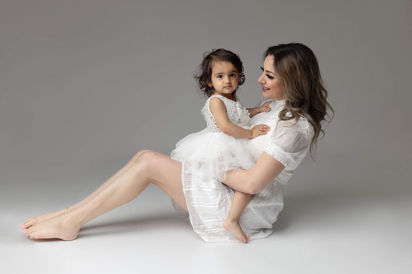 Two people wearing white outfits pose gracefully together in an artistic dance-like sequence on a light gray backdrop.
