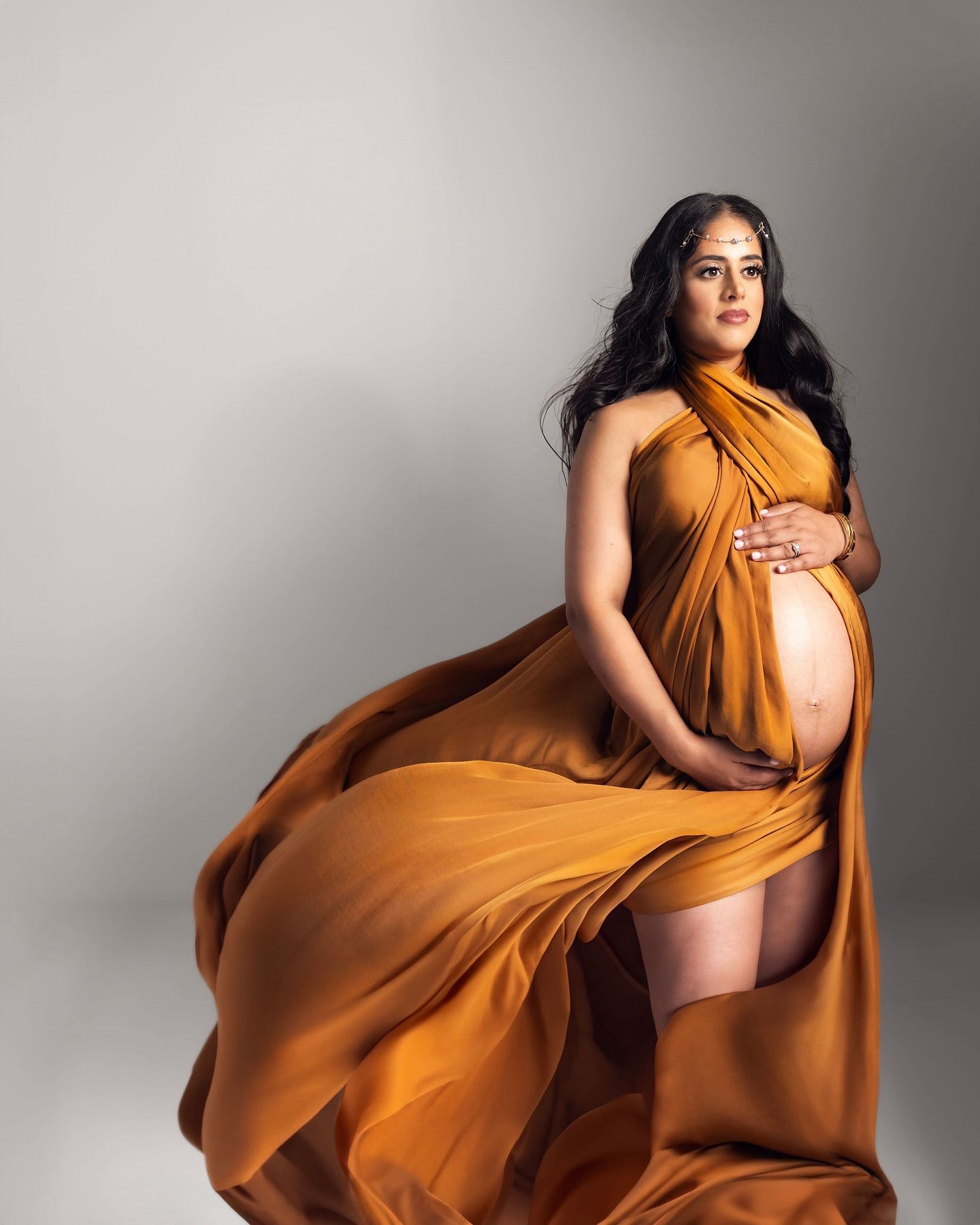 Maternity photoshoot series showing flowing orange dress movement against gray studio backdrop in artistic poses.