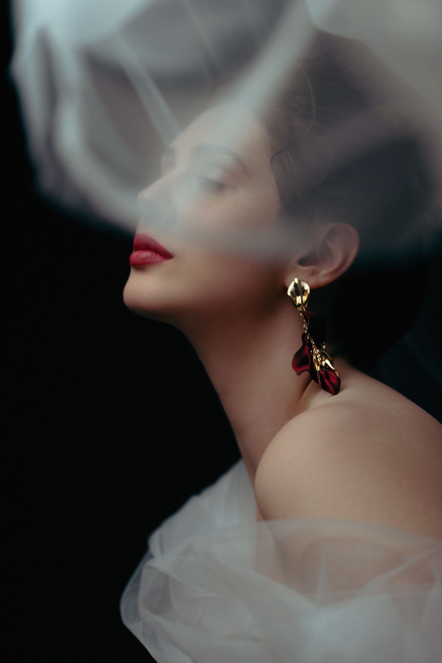 Artistic portrait with delicate veil and ornate earrings in dramatic lighting.