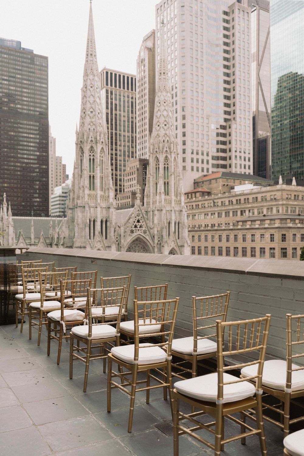 Gold chiavari chairs with white cushions arranged on a rooftop terrace with St. Patrick's Cathedral in the background.