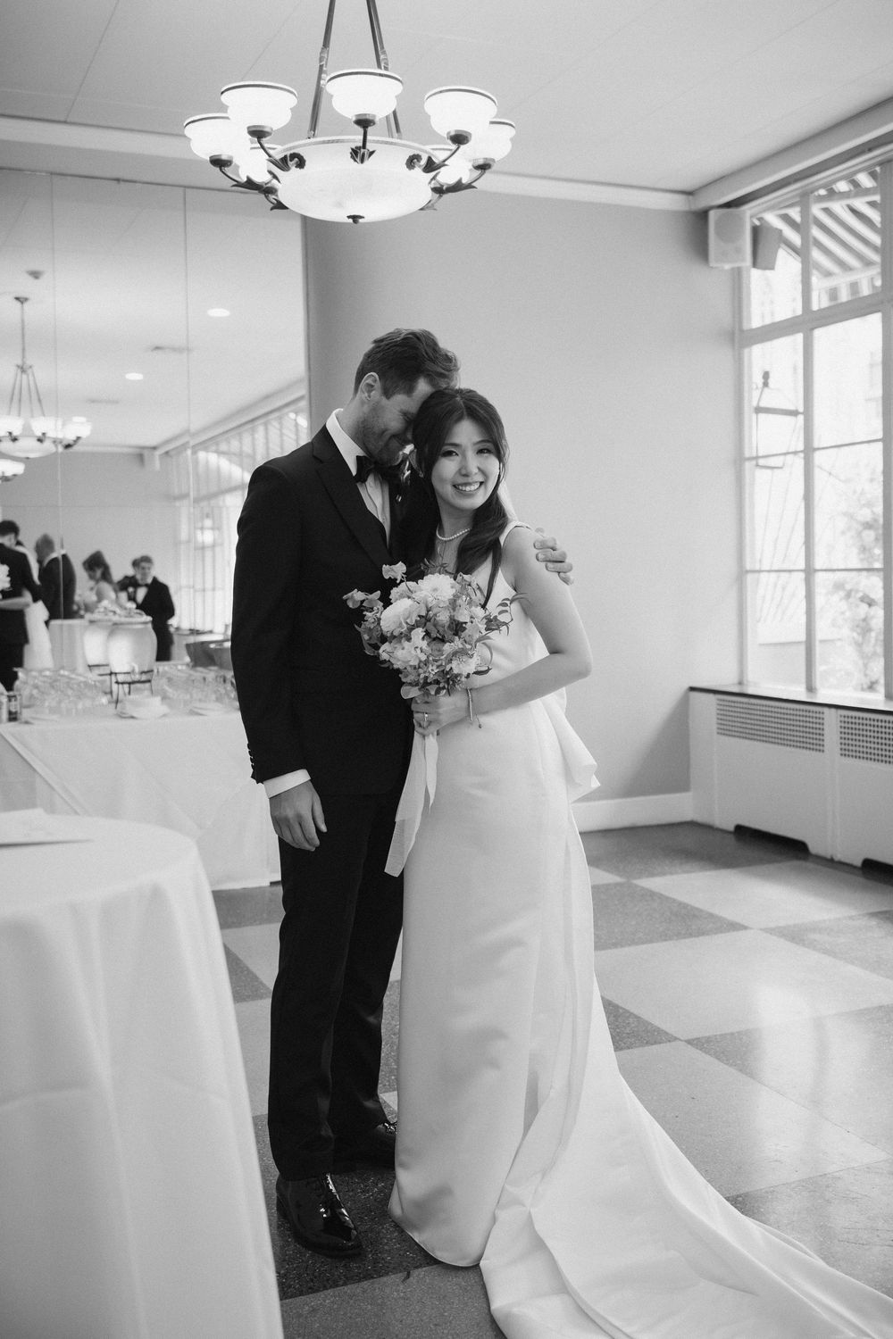 Wedding couple sharing romantic moments in an elegant white reception room with chandeliers.