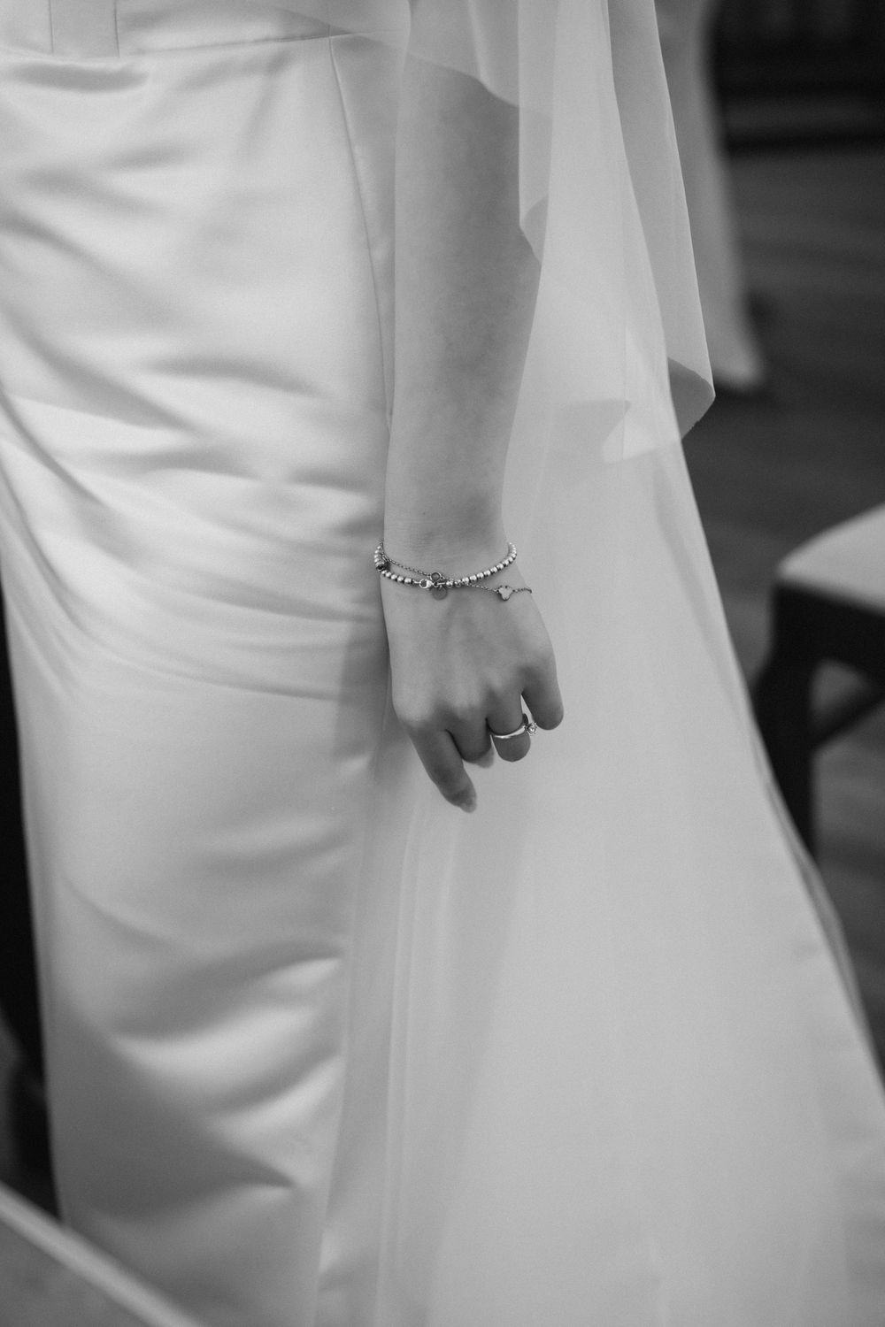Close-up details of a flowing white wedding dress and delicate jewelry.