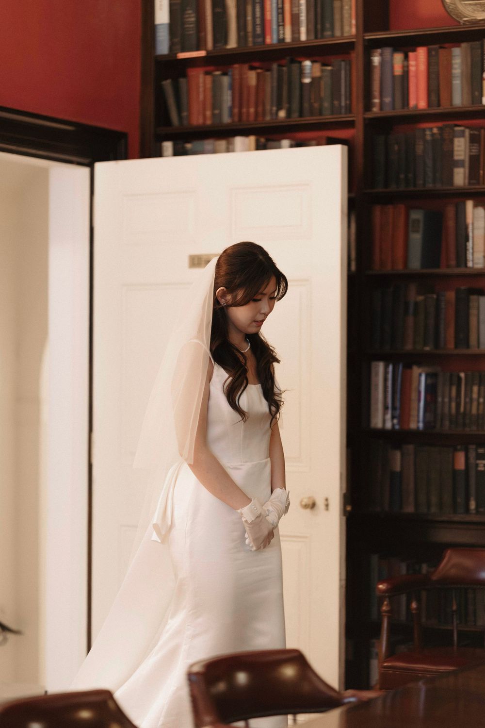 Wedding dress detail in a library setting with red walls and wooden bookshelves.