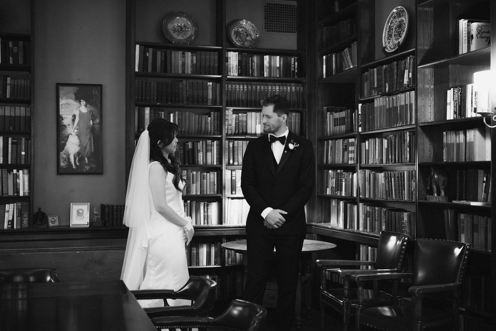 Black and white photograph of a wedding ceremony in a grand library setting.
