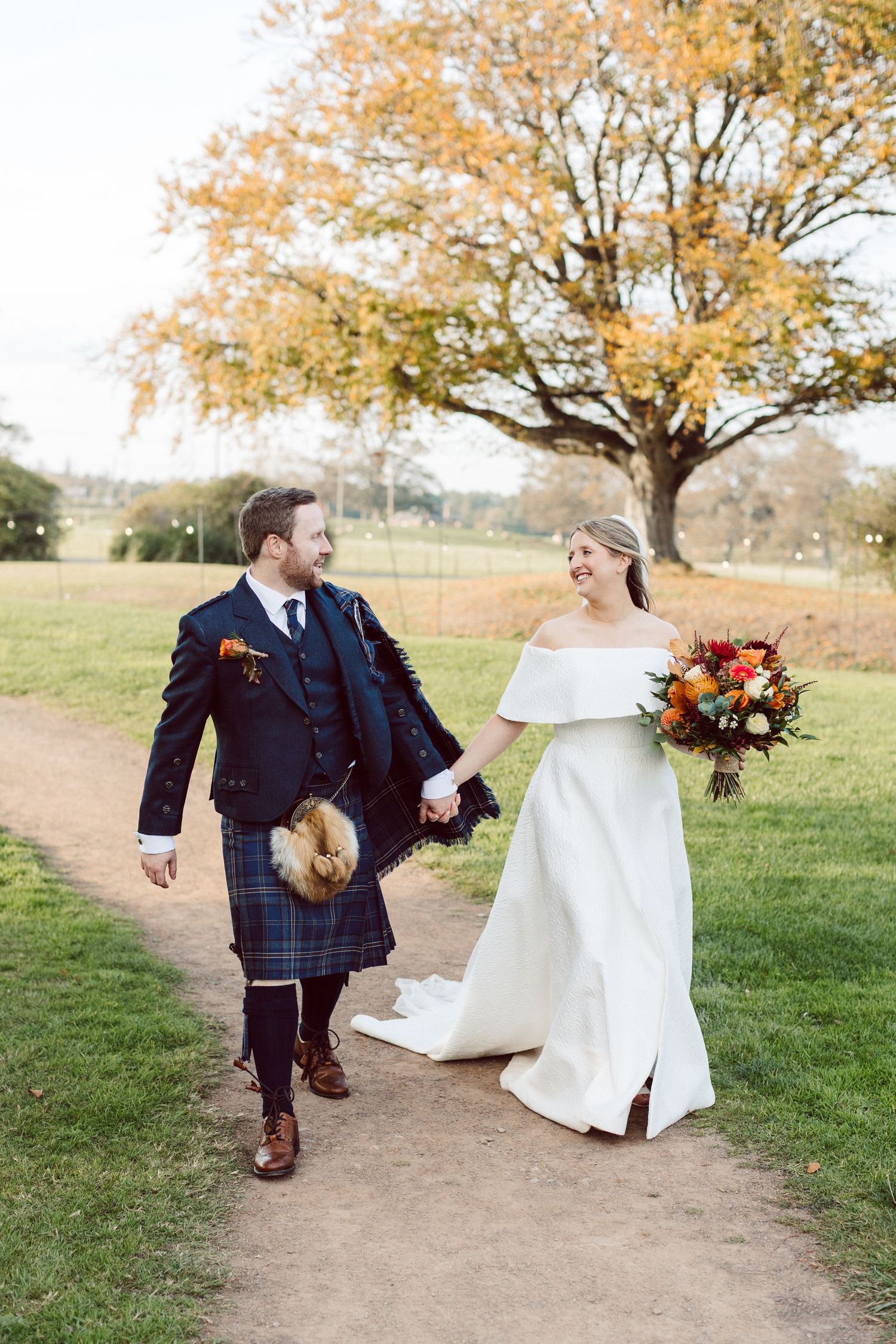 Autumn wedding photos with couple walking under golden-leaved trees.