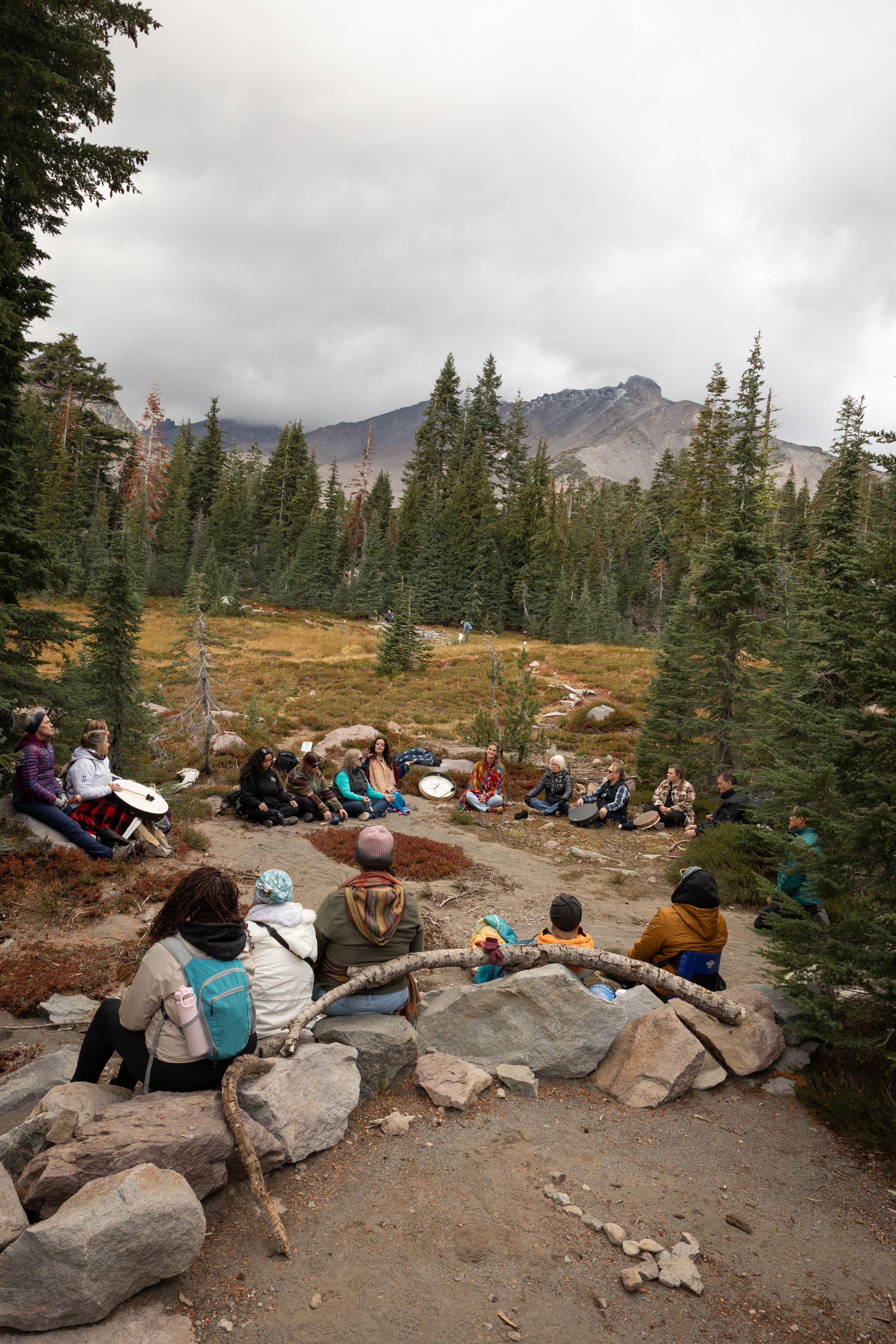 A group of hikers resting on rocky outcrops with evergreen trees and mountain views in the background.