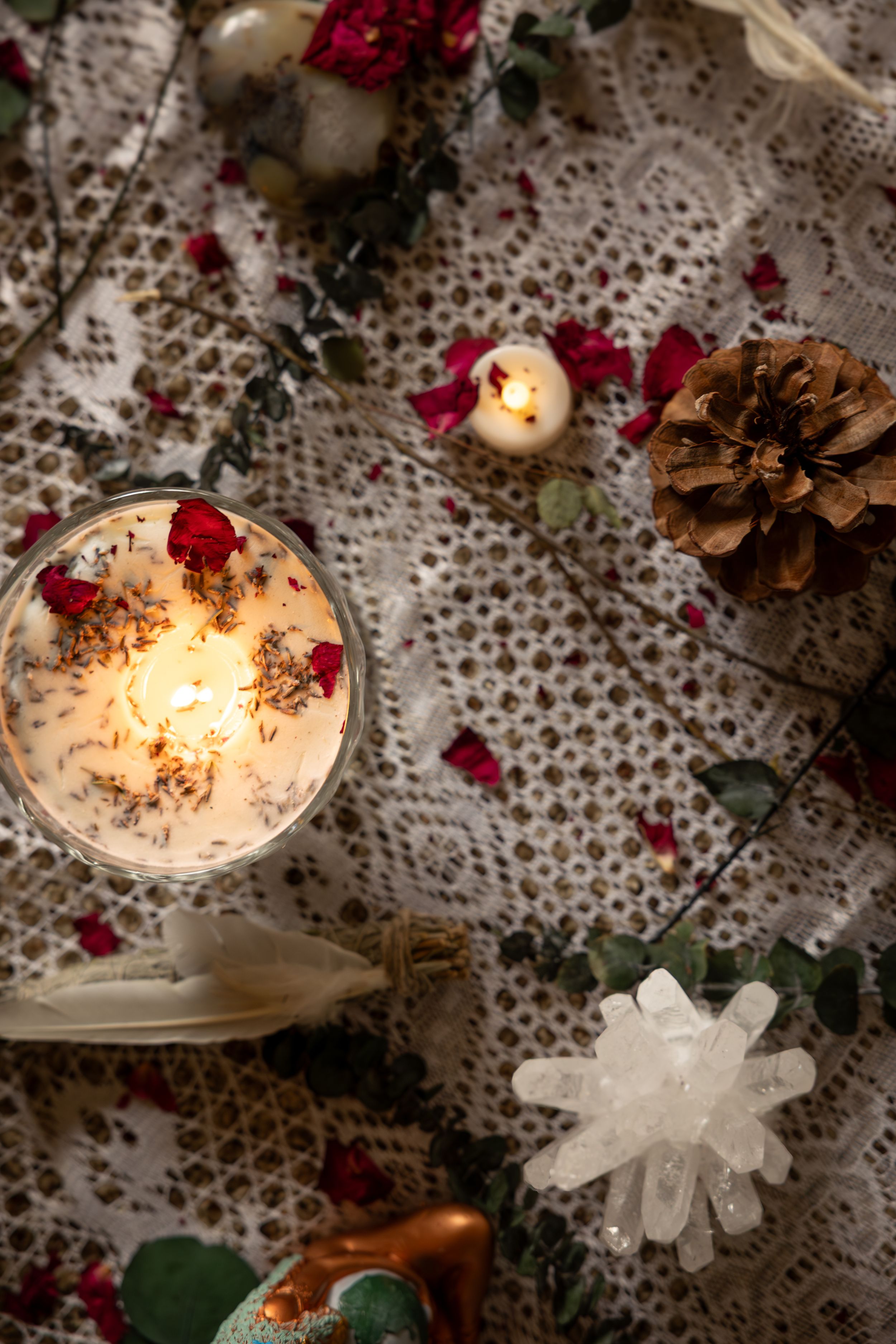 Glowing candles with red flowers and pine cones on white lace tablecloth create a romantic holiday atmosphere.