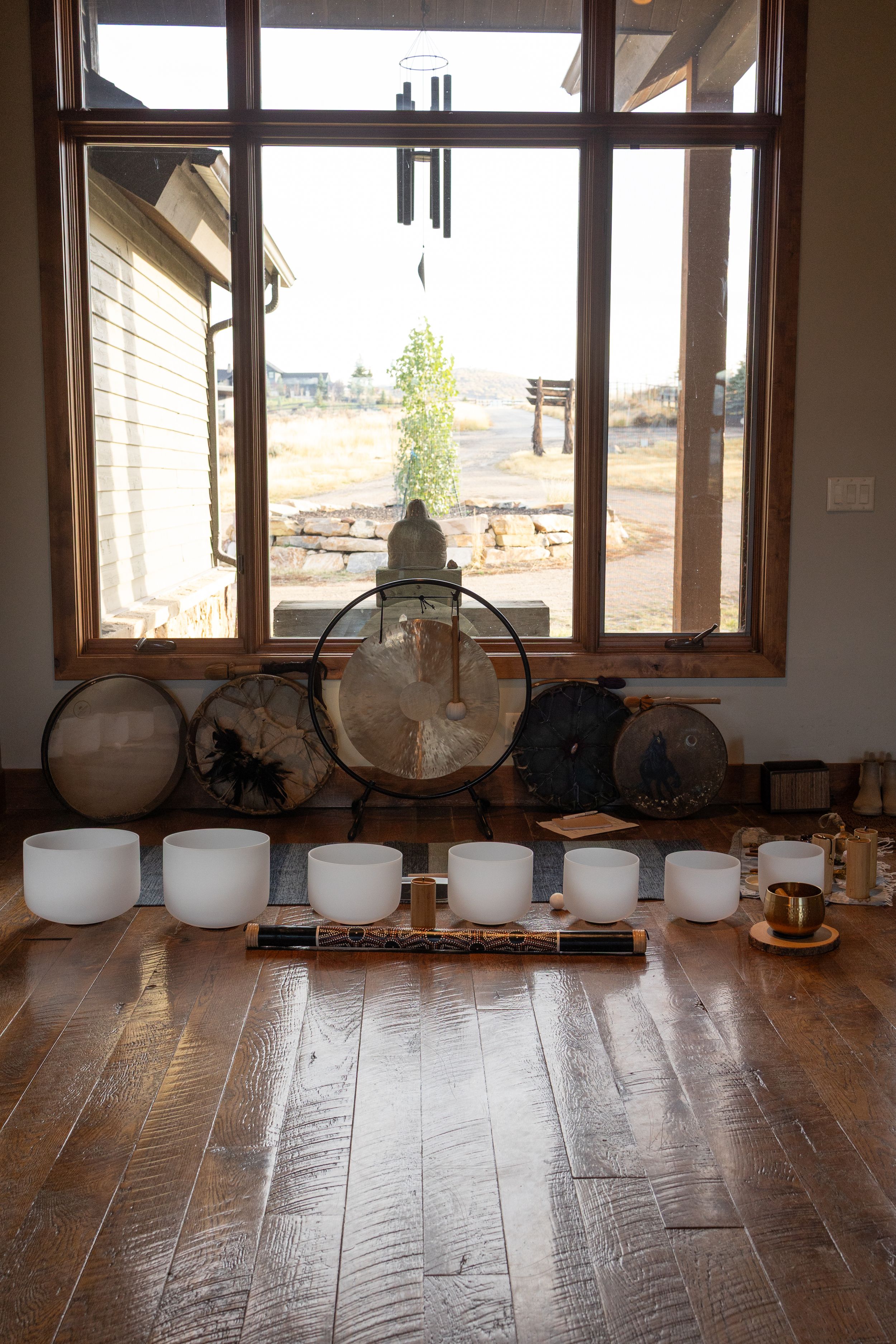 Row of white crystal singing bowls arranged on wooden floor near windows in meditation or yoga studio.