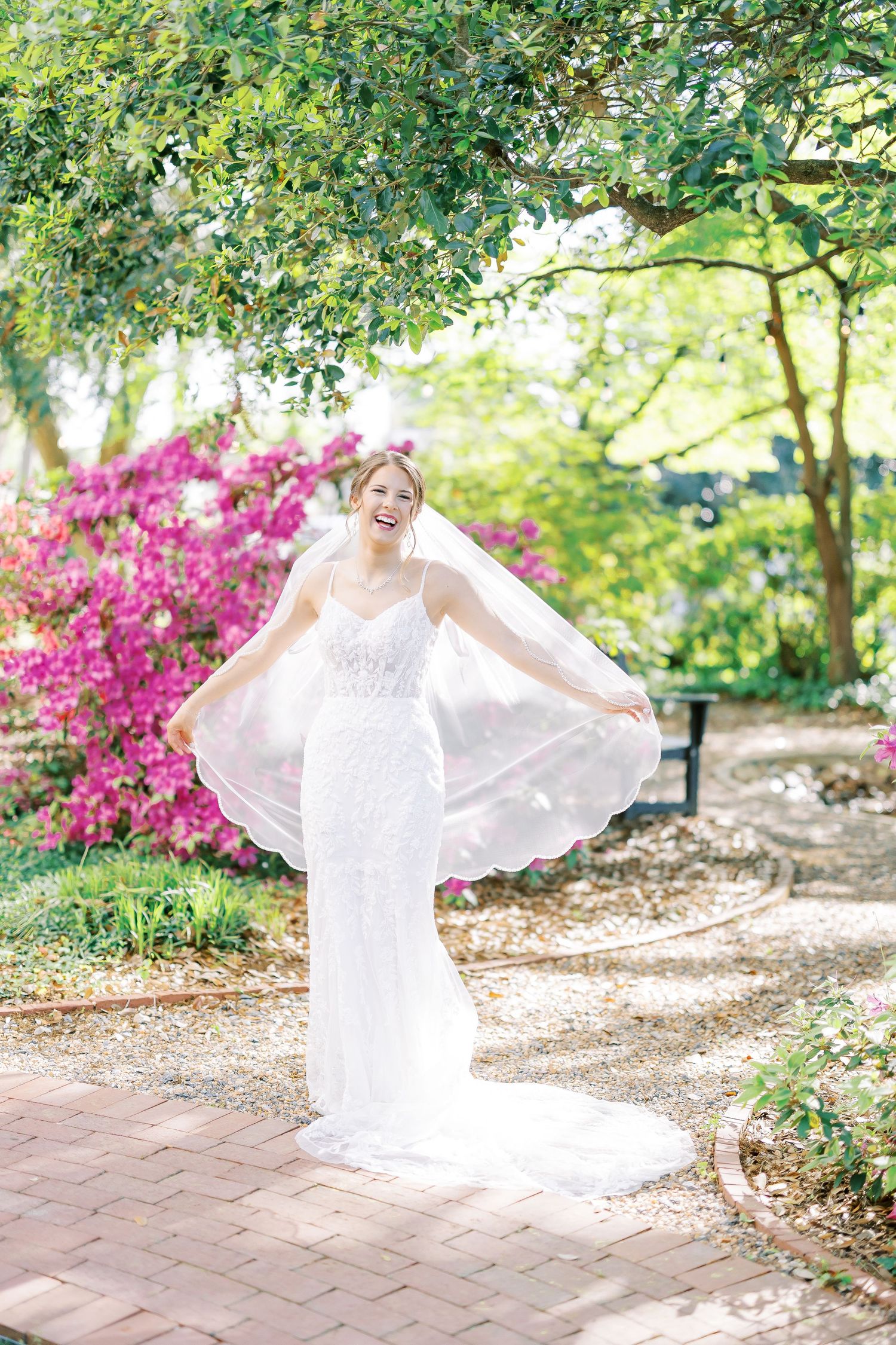 A flowing white dress twirls gracefully in a garden setting with vibrant pink azalea bushes and stone pathways.