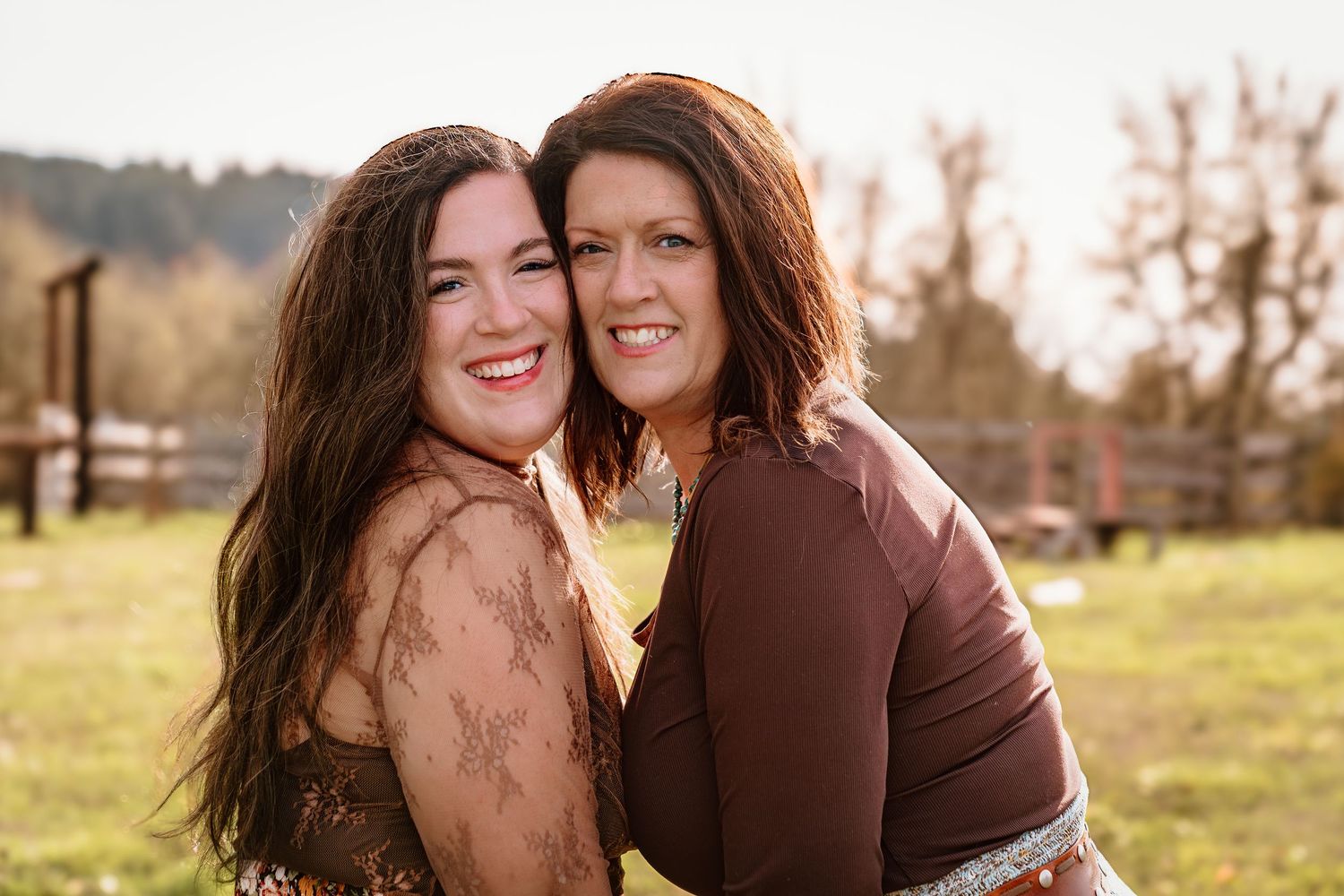 Two friends embracing and laughing together in sunlit field during golden hour.