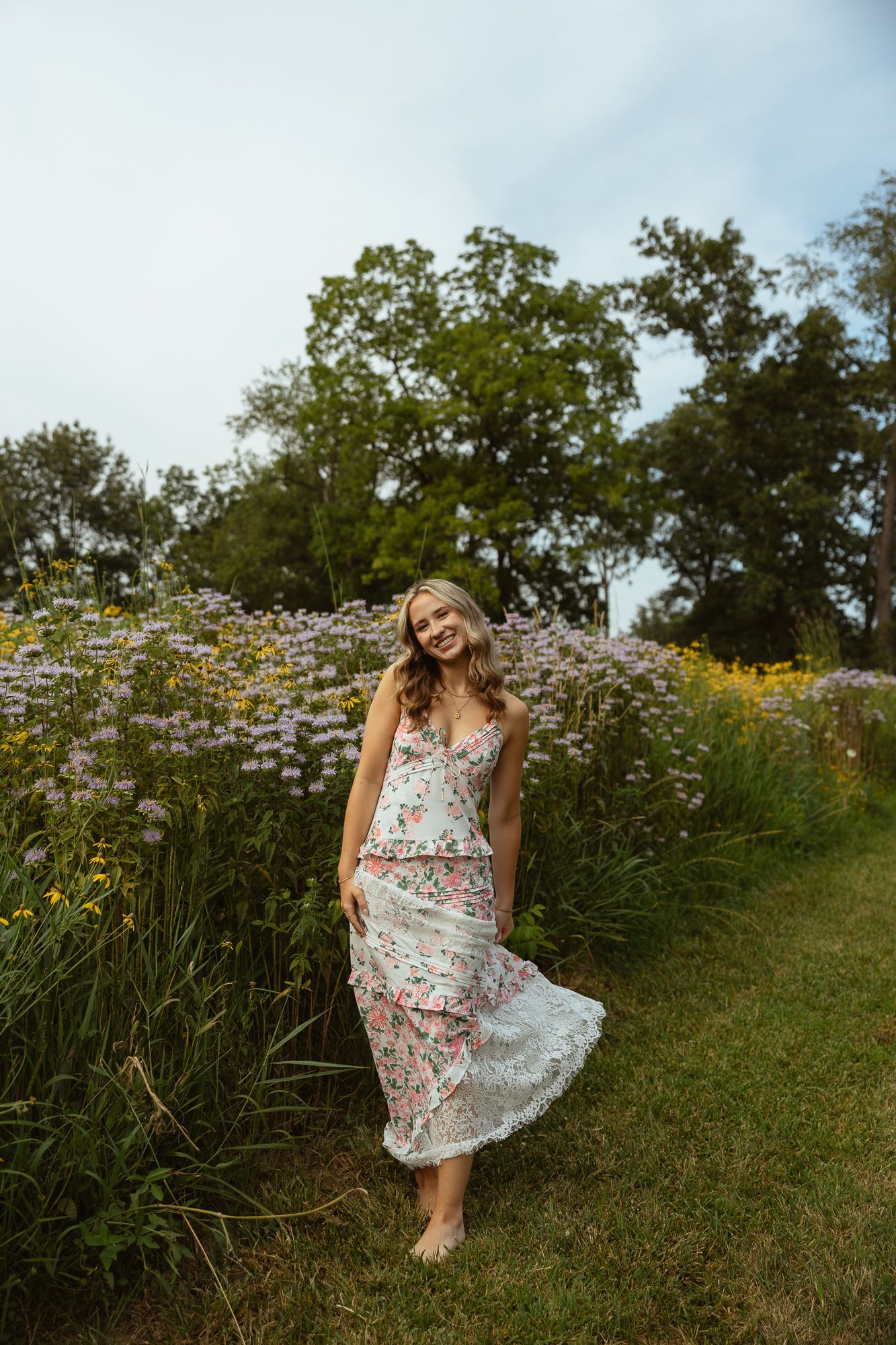 A woman in a floral dress twirls joyfully in a wildflower meadow during golden hour.