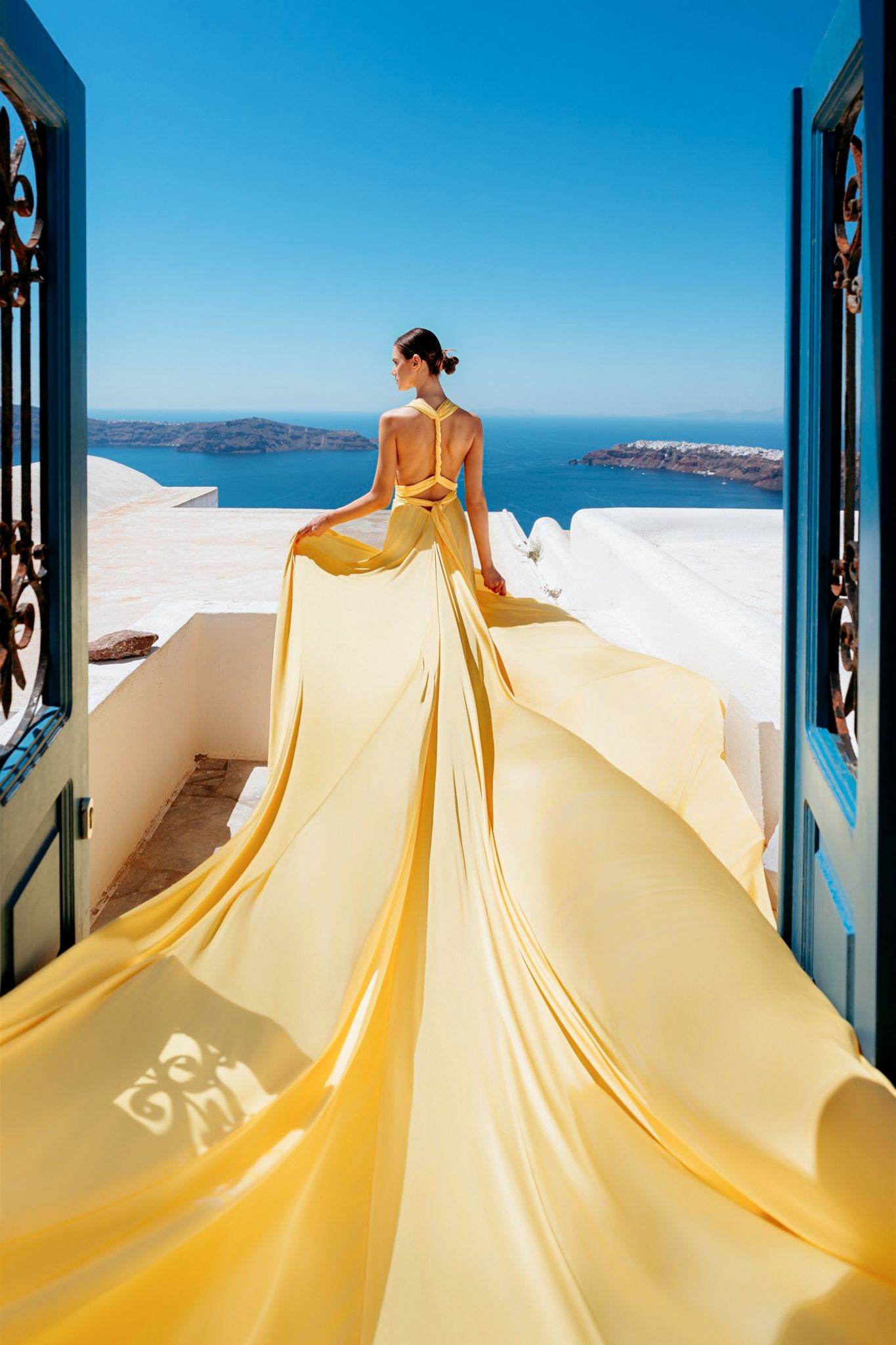 Two flowing dresses in red and purple billow dramatically against white Greek architecture and blue sky in Santorini.
