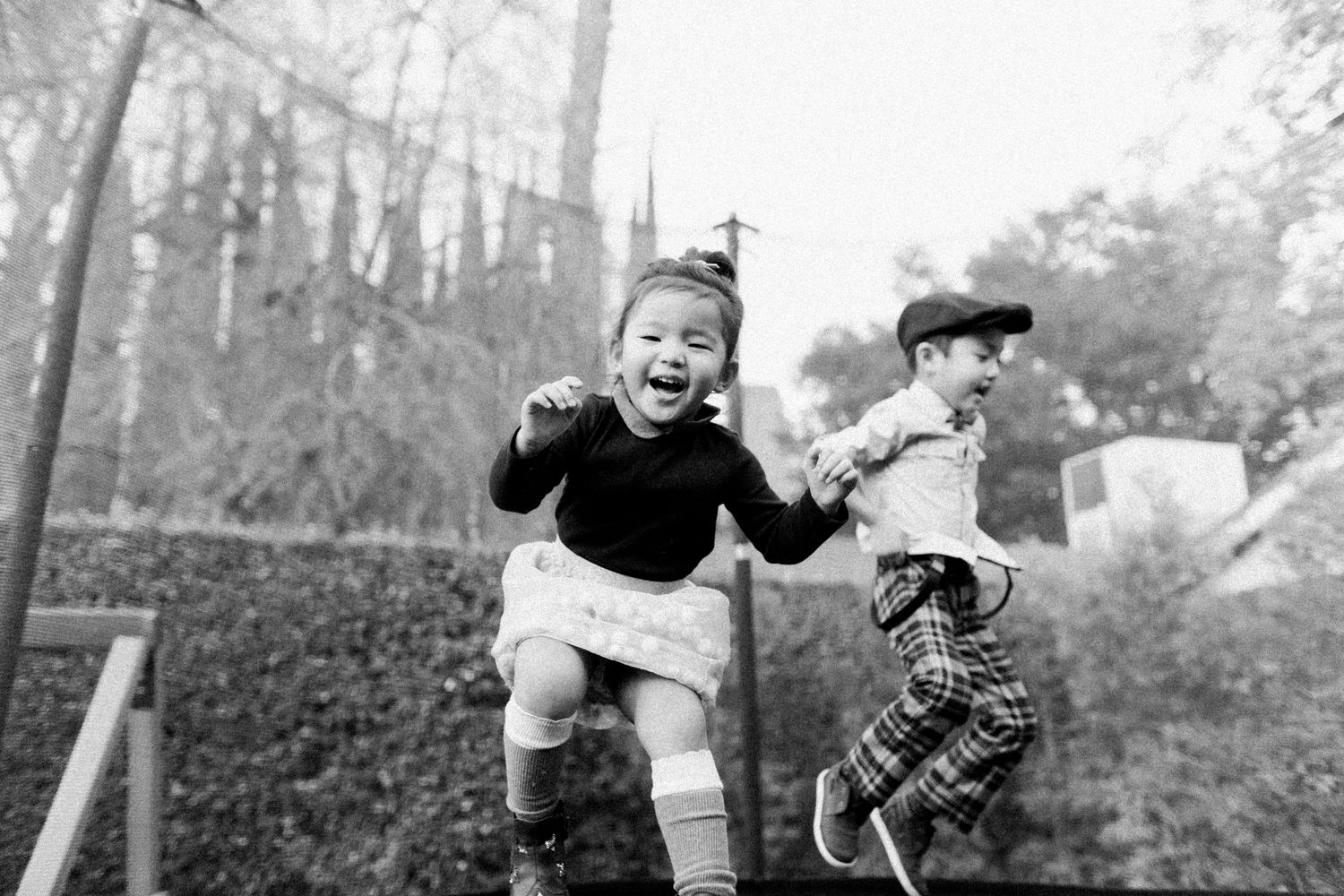 little girl and boy jumping on a trampoline, black and white