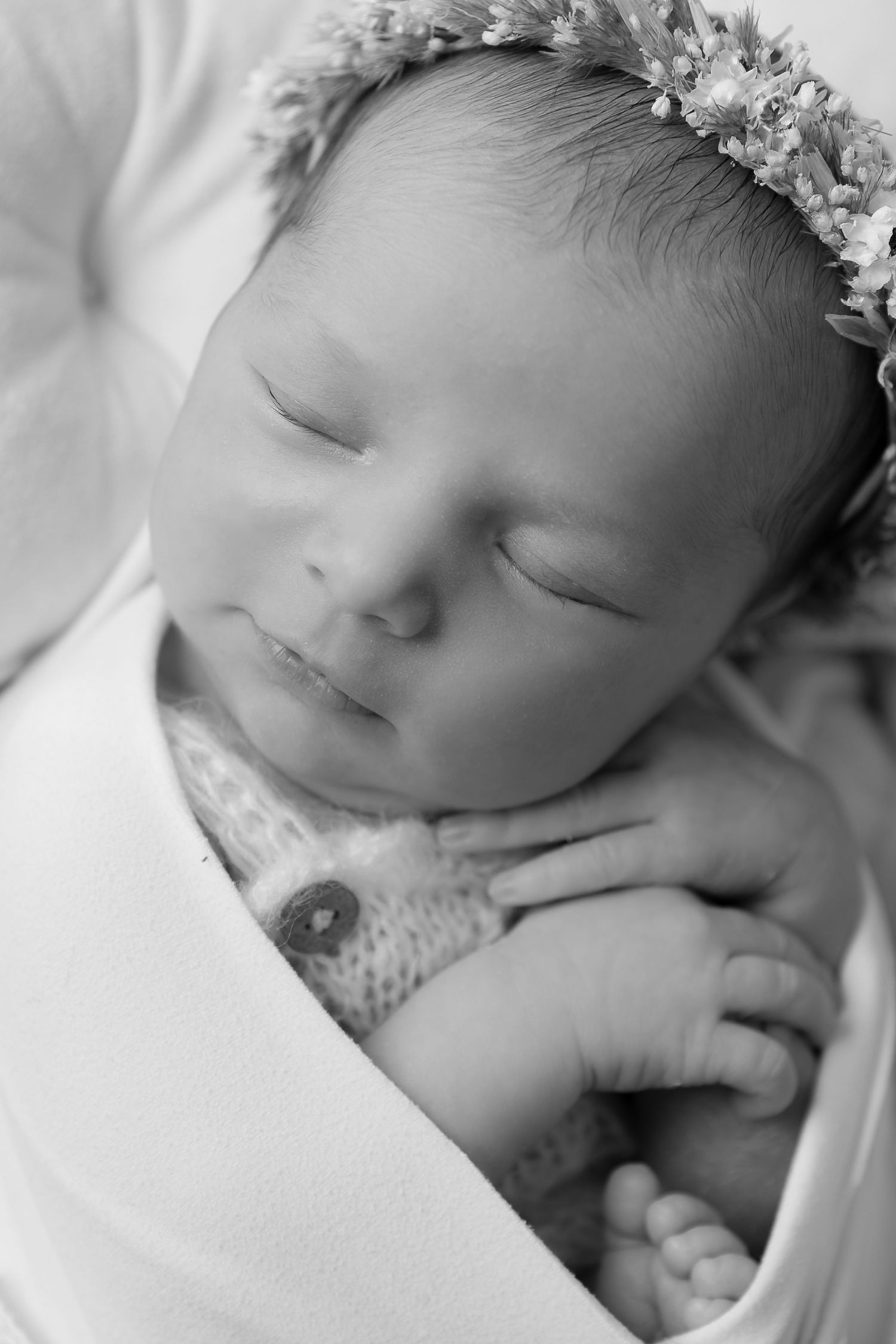 Peaceful sleeping newborn wearing floral crown and cuddling small stuffed toy.