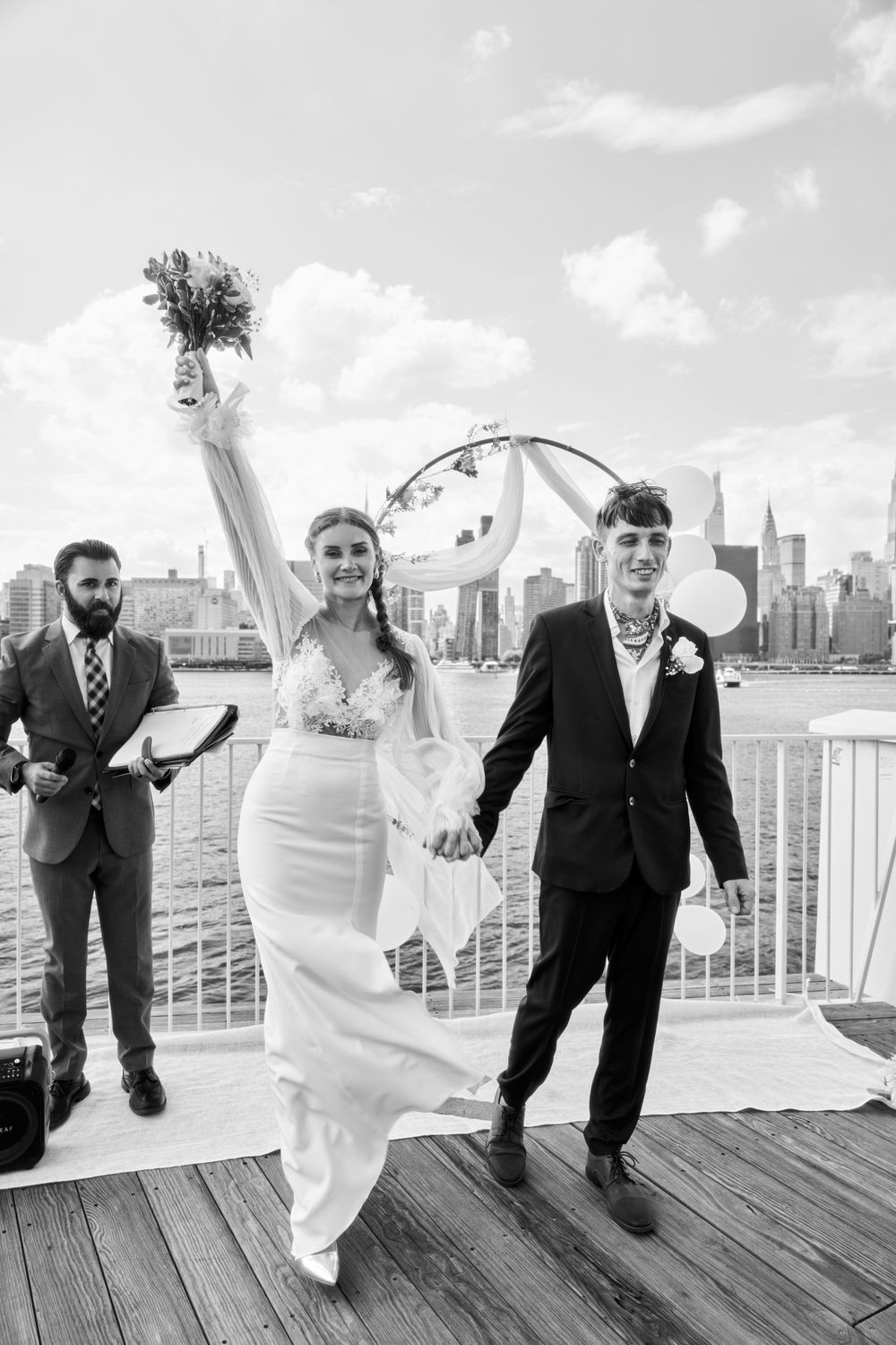 Wedding party having fun jumping in sequence on a dock with city skyline in the background.