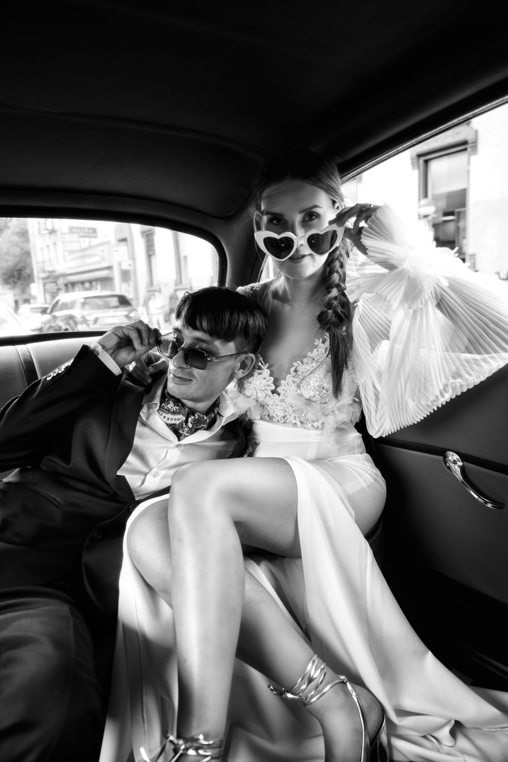 Wedding couple in vintage-style photo shoot inside classic car with sunglasses.