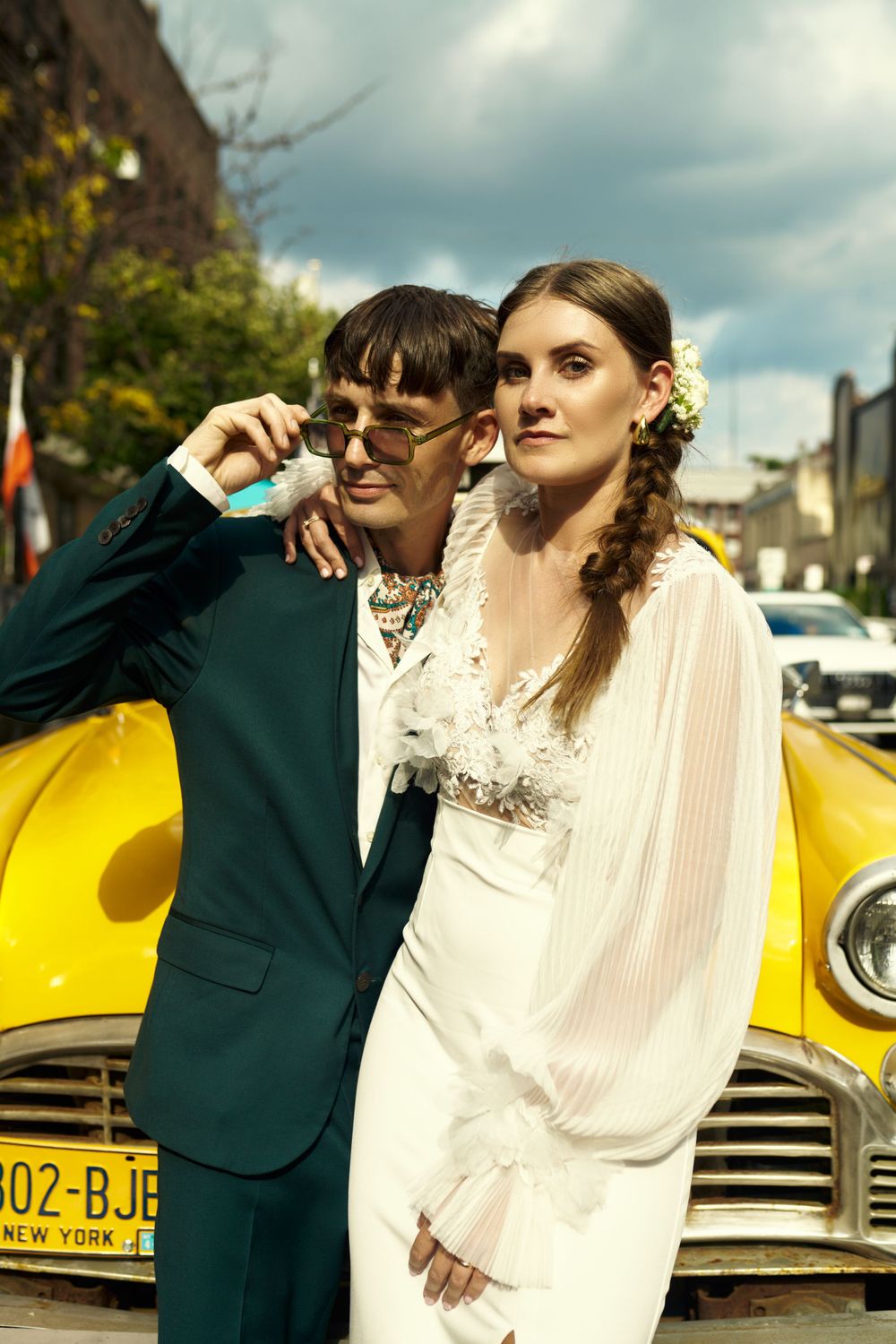 Stylish wedding couple poses against vintage yellow taxi cab on city street.