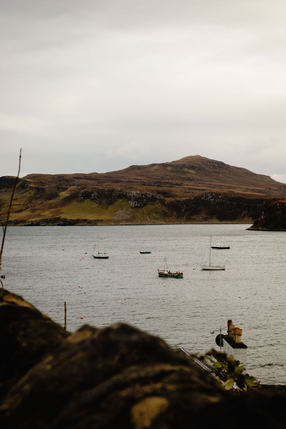 Small boats anchored in a tranquil bay with rugged hills and mountains in the background.