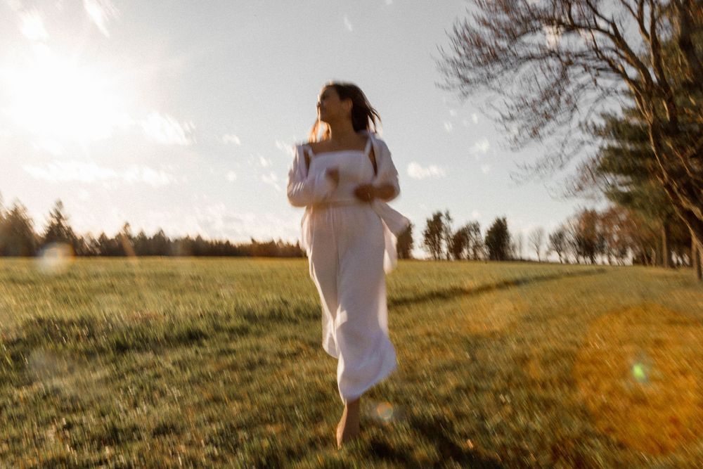 Person in flowing white dress running through sunlit field at golden hour.