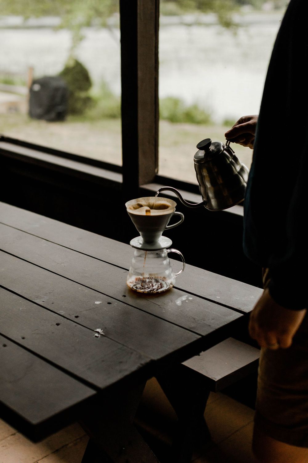 Pour-over coffee being prepared by window with lake view in cozy cabin setting.