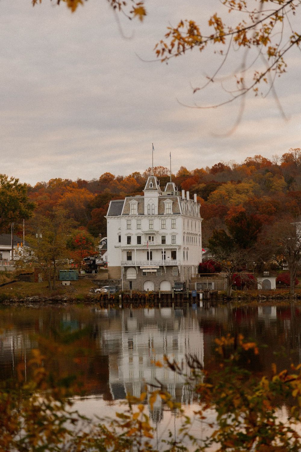 White Victorian mansion reflected in calm lake waters surrounded by fall foliage.