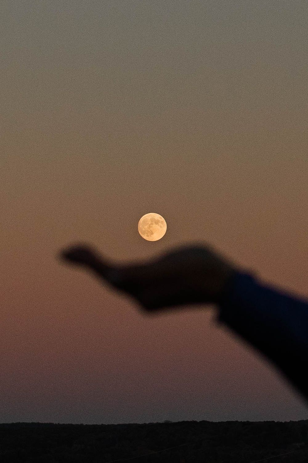Full moon in dusky sky with silhouetted hand appearing to hold it.