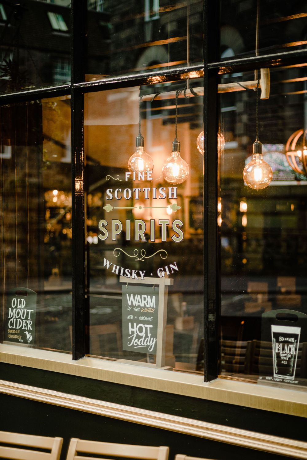 Illuminated storefront window displaying 'Fine Scottish Spirits' sign with vintage light bulbs.