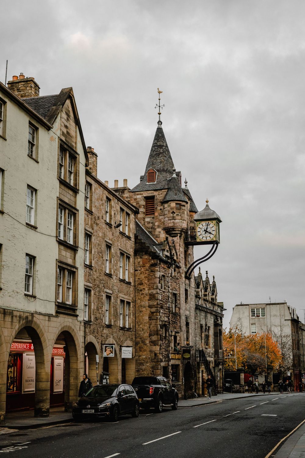 Historic Edinburgh street with classic stone architecture and clock tower under cloudy skies.