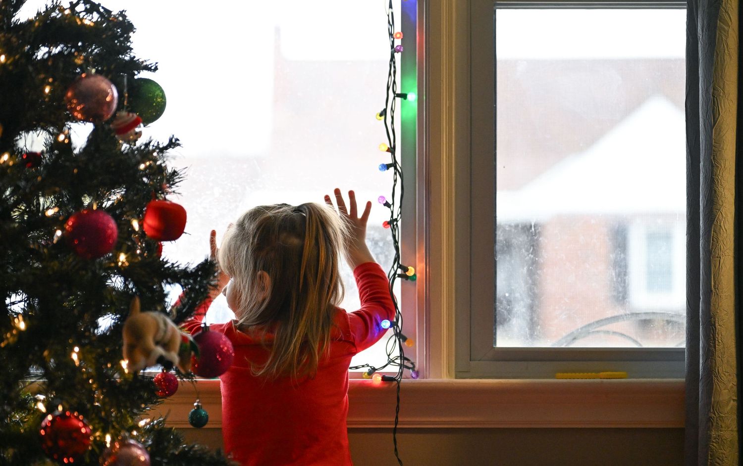 A color photo of Emma standing by the Christmas tree in the living room, looking out the front window of the house