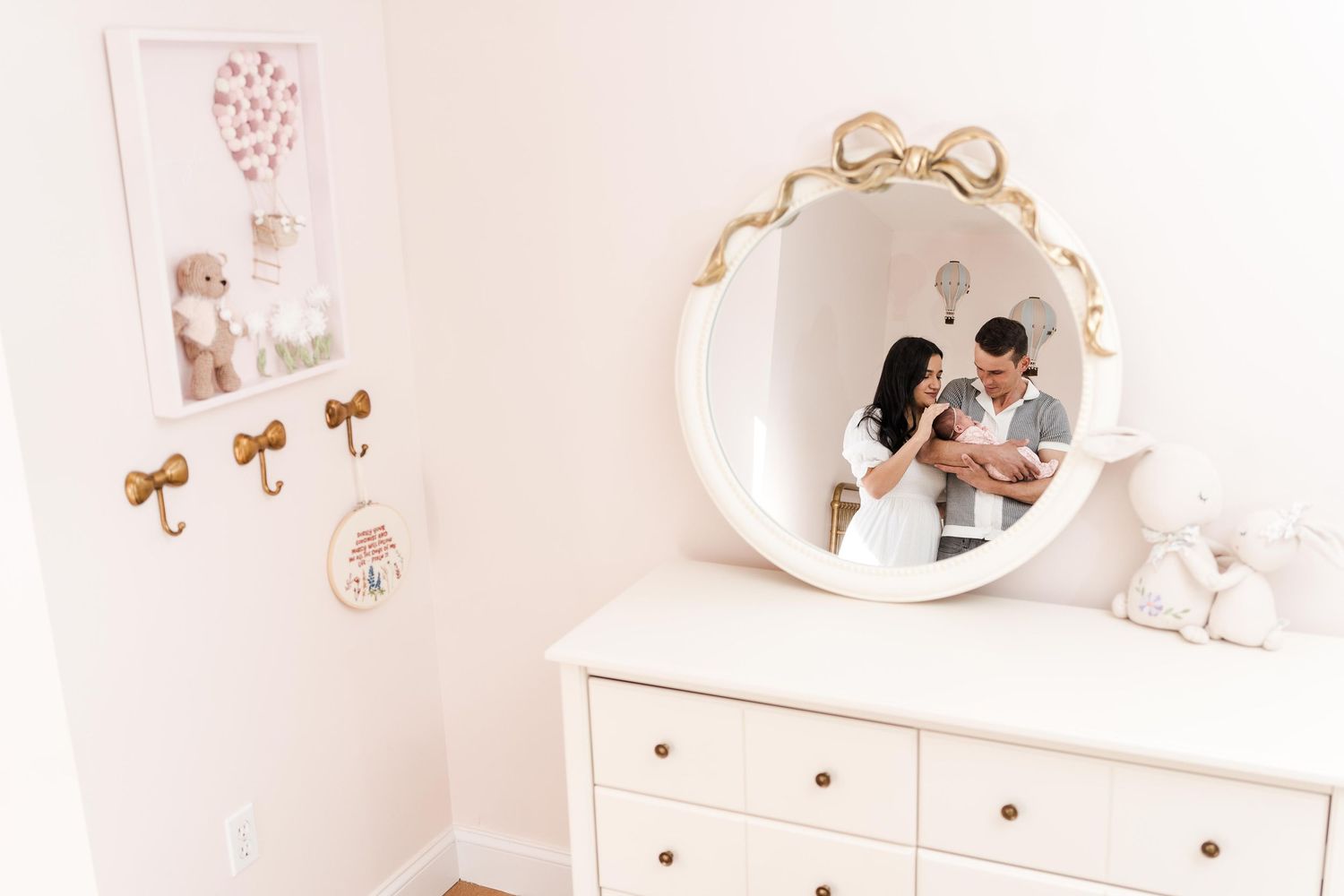 Elegant white nursery room with gold accents featuring a dresser, mirror, and delicate floral wall decals.