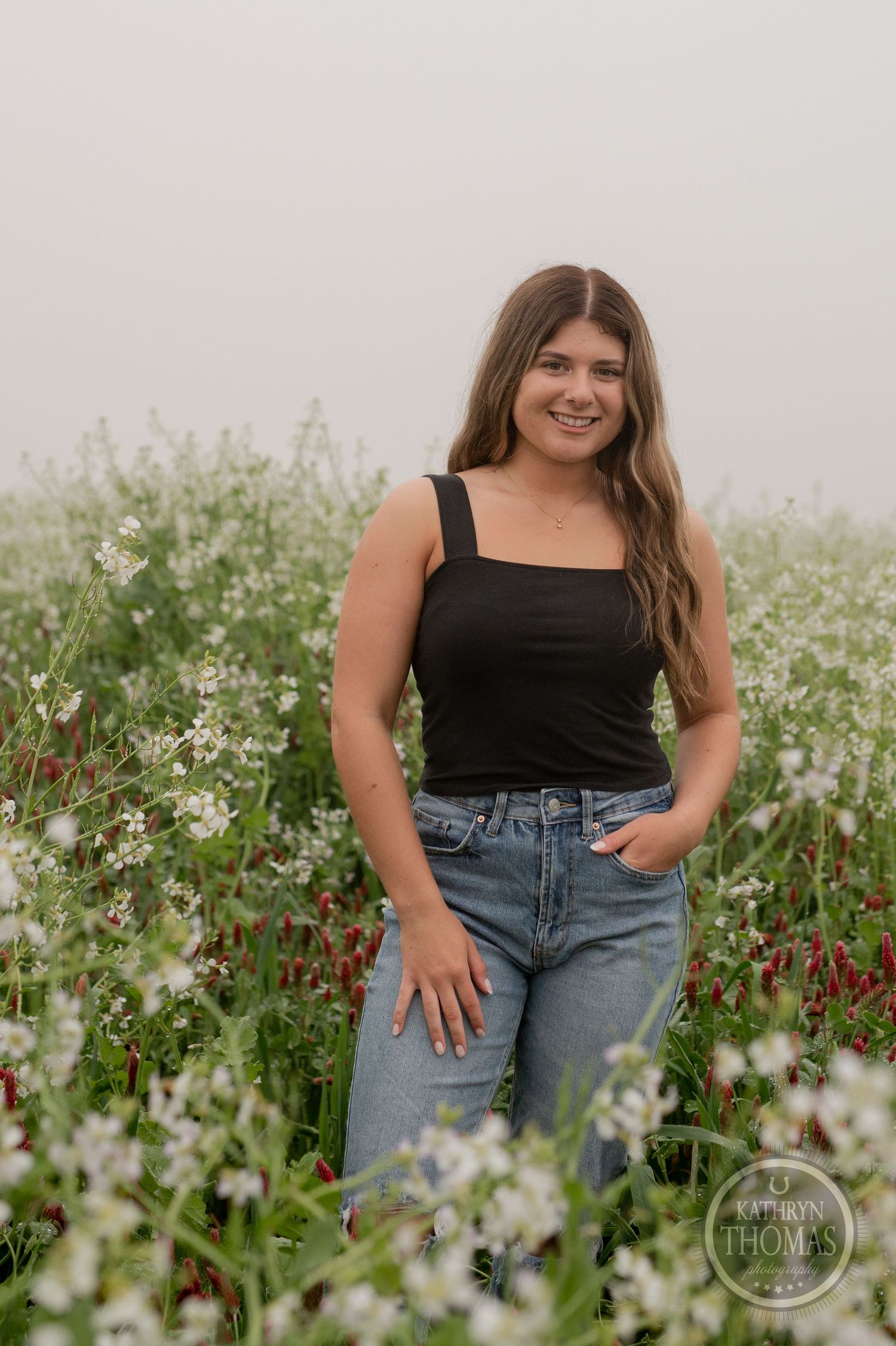 A casual portrait in a wildflower field wearing a black tank top and jeans among white and red blooms.