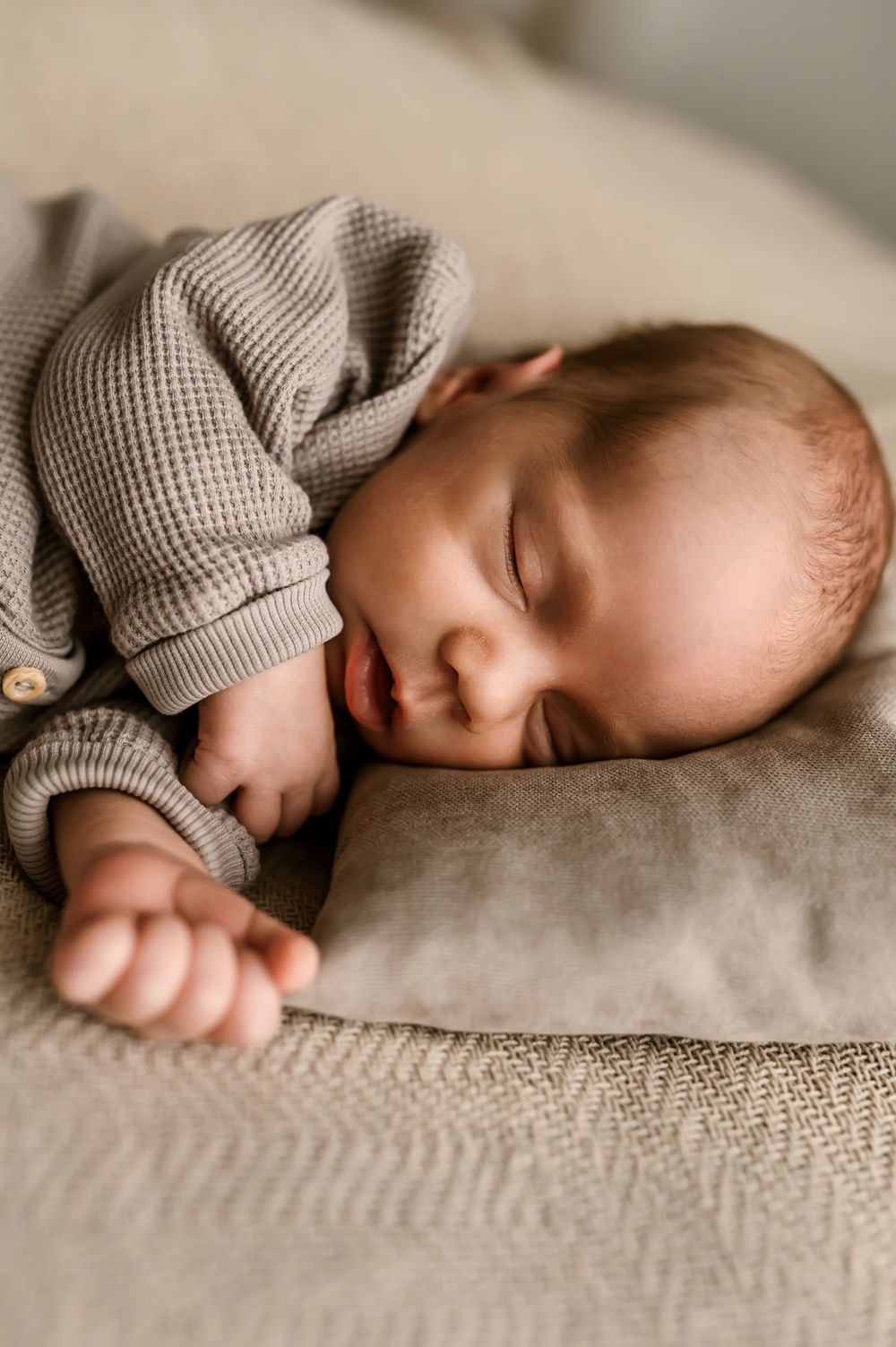 A peaceful baby sleeping on soft beige bedding while wearing a cozy gray knit sweater.