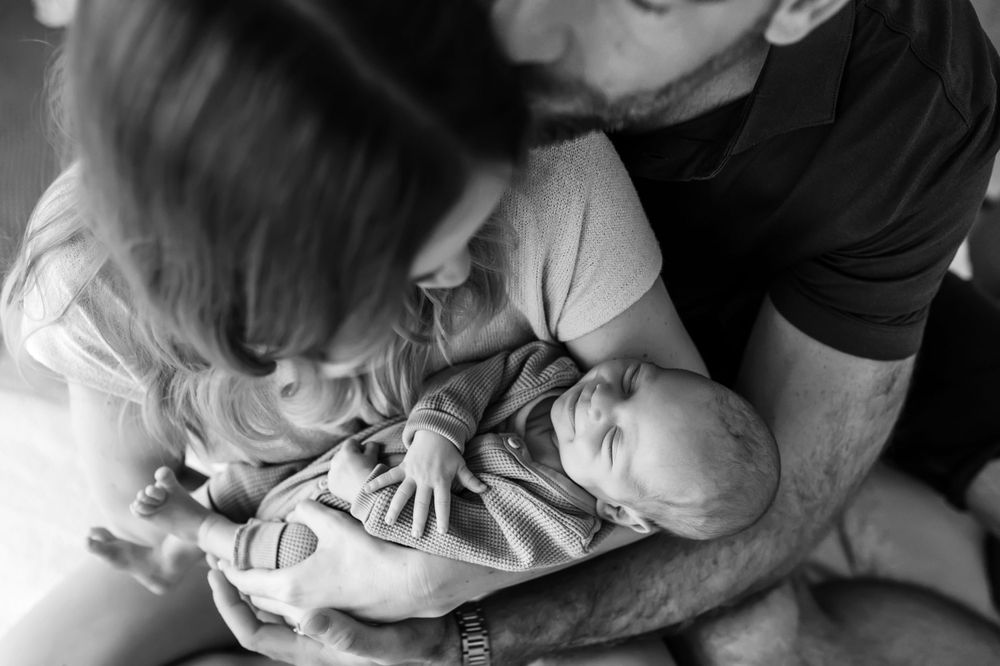 Black and white photo showing tender moment between a newborn baby and parents in intimate embrace.